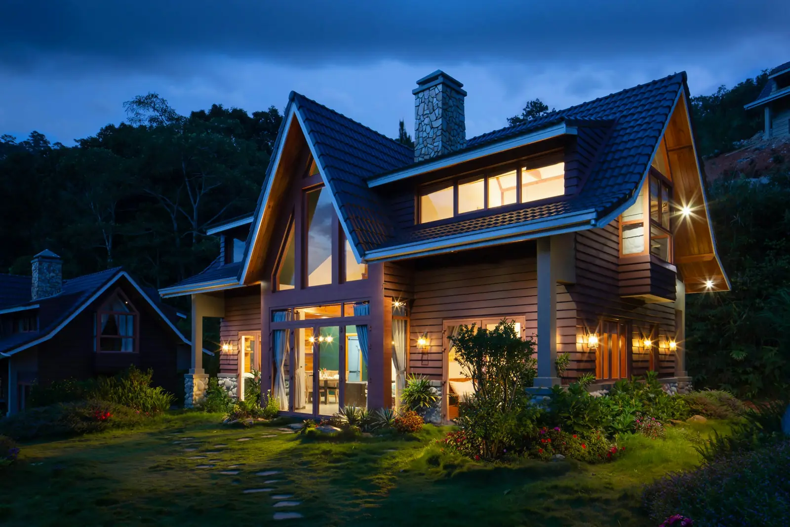 A large weatherboard home with a tiled roof, lit up at dusk